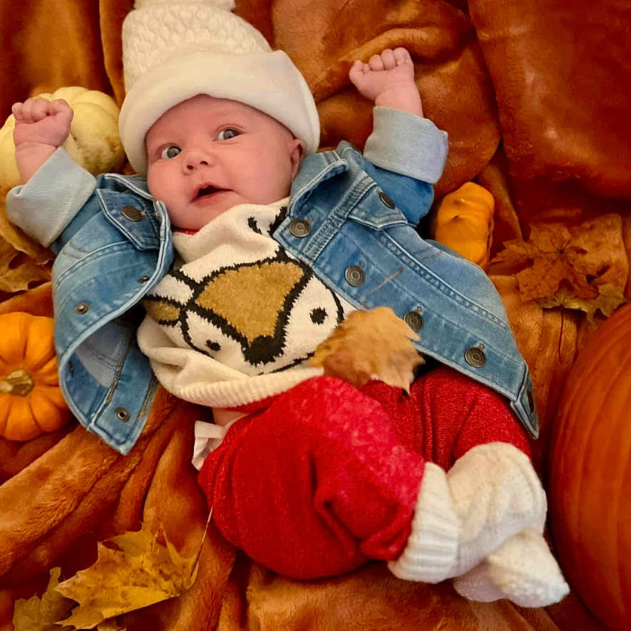 Delilah is registered to the contest to win money with this photo: baby, bodypart, bonnet, cap, clothing, coat, couch, face, finger, furniture, glove, hat, head, jacket, jeans, newborn, pants, person, photography, portrait