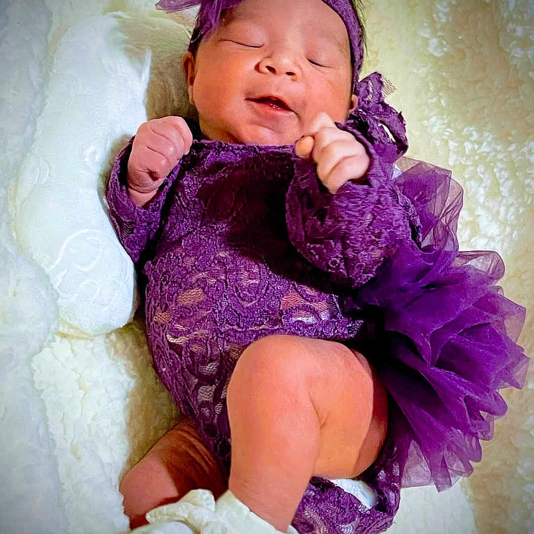 Zaya is registered to the contest to win money with this photo: baby, blanket, child, closeup, cozy, cute, headband, indoors, infant, newborn, peaceful, portrait, purple_clothing, resting, sleeping, small_hands, smiling, soft_texture, tutu, white_booties