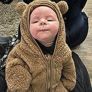 Aiden is registered to the contest to win money with this photo: baby, infant, child, fuzzy_clothing, bear_onesie, cute, face, expression, indoor, carpet, seat, zipper, warm_clothing, person, portrait, soft_texture, head, hands, sitting, cozy