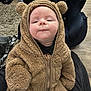 baby, infant, child, fuzzy_clothing, bear_onesie, cute, face, expression, indoor, carpet, seat, zipper, warm_clothing, person, portrait, soft_texture, head, hands, sitting, cozy
