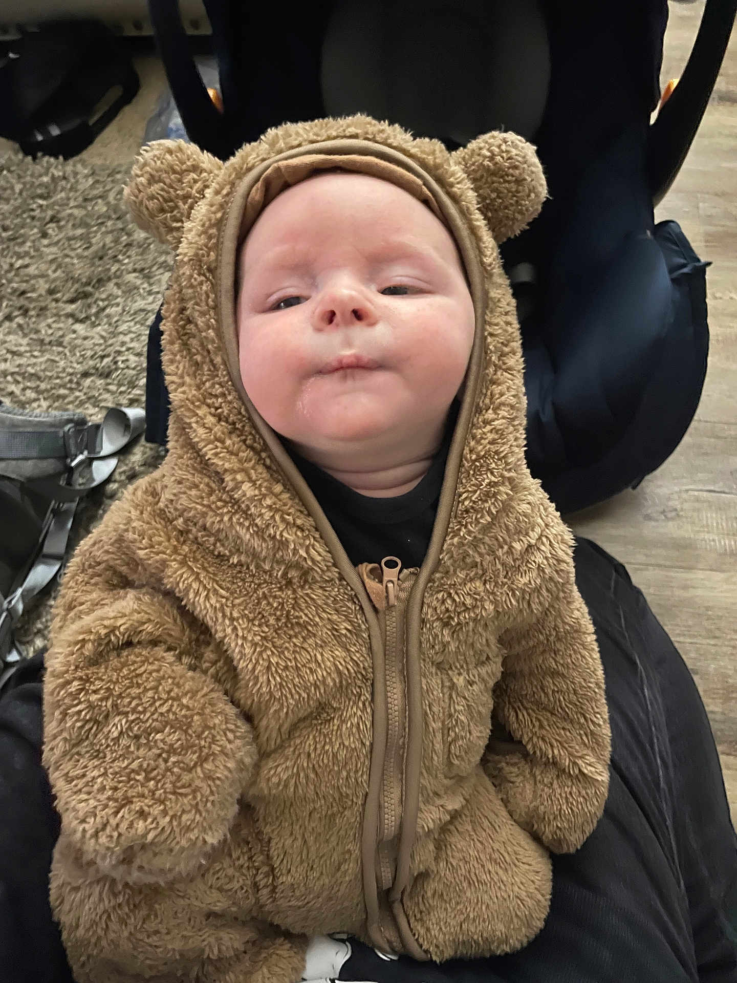 Aiden is registered to the contest to win money with this photo: baby, infant, child, fuzzy_clothing, bear_onesie, cute, face, expression, indoor, carpet, seat, zipper, warm_clothing, person, portrait, soft_texture, head, hands, sitting, cozy