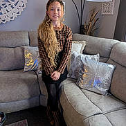 Julia is registered to the contest to win money with this photo: child, girl, long_hair, standing, smiling, houndstooth, sweater, boots, headband, living_room, sofa, cushions, decor, lamp, carpet, wall_art, indoor, portrait, fashion, person