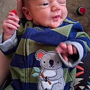 Michael Lewis joined the competition — help win amazing prizes! baby, infant, newborn, face, hand, onesie, koala_patch, striped_clothing, toy, ball, carpet, adult_hand, close_up, portrait, indoor, blanket, sleepy, cute, smiling, tiny_fingers