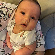 Tate is registered to the contest to win money with this photo: baby, infant, child, onesie, animal_print, tattoo, hand, cushion, blanket, cat_design, indoor, person, cute, chubby_cheeks, portrait, looking_at_camera, skin, soft_lighting, cozy, seated