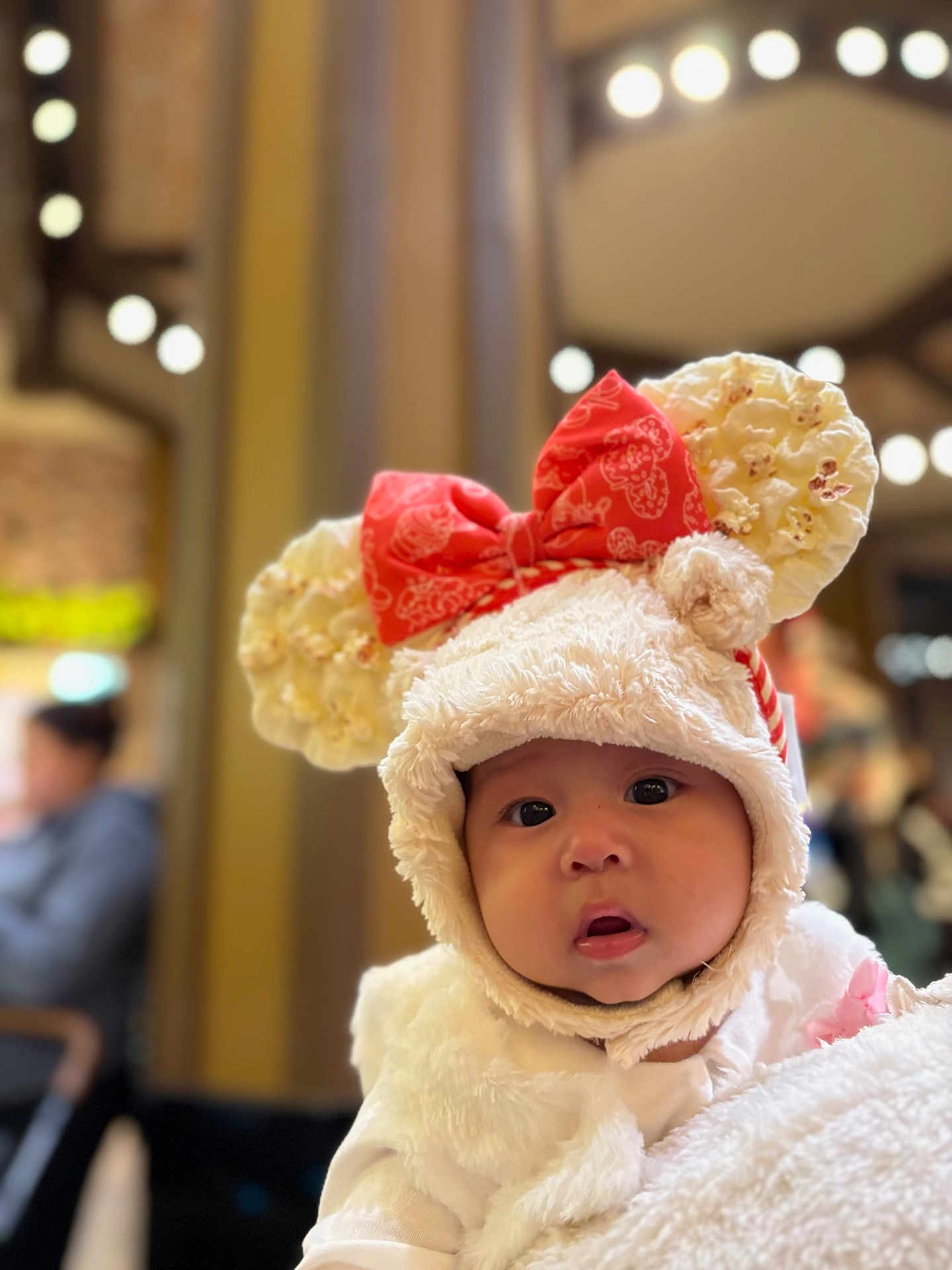 Sayda joined the competition — help win amazing prizes! baby, child, hat, popcorn, red_bow, fluffy_clothing, portrait, indoor, blurred_background, lights, cute, face, wide_eyes, white, soft_texture, warm_lighting, person, infant, headwear, curious_expression