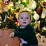 Lizyo participe au concours pour gagner de l'argent avec cette photo : toddler, child, indoor, christmas_tree, holiday, decorations, wooden_chair, green_sweater, curious, face, young_child, festive, lights, ornaments, home, smiling, person, seated, cute, holiday_season