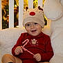 baby, child, reindeer_hat, red_onesie, candy_cane, smiling, christmas, holiday_lights, festive, cute, sitting, sock, plush_chair, indoors, portrait, happy, toddler, seasonal, cozy, celebration