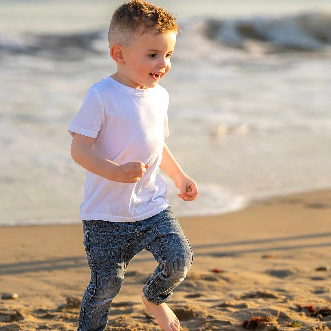 Raphaël participe au concours pour gagner de l'argent avec cette photo : barefoot, beach, blue_jeans, boy, casual_clothing, child, daytime, happy, joyful, ocean, outdoor, playful, running, sand, smiling, summer, sunlight, waves, white_tshirt, young