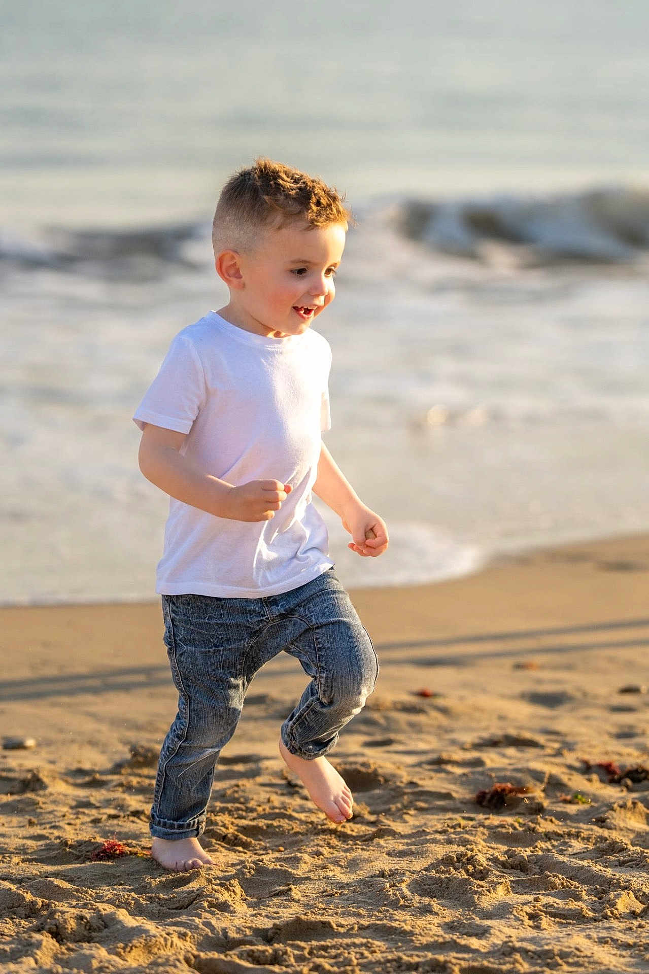 Raphaël participe au concours pour gagner de l'argent avec cette photo : barefoot, beach, blue_jeans, boy, casual_clothing, child, daytime, happy, joyful, ocean, outdoor, playful, running, sand, smiling, summer, sunlight, waves, white_tshirt, young