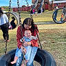 baby, child, guardian, playground, tire_swing, swing, outdoor, park, smiling, happy, family, cuddle, infant, blue_sky, grass, barn, slide, playground_equipment, daylight, portrait