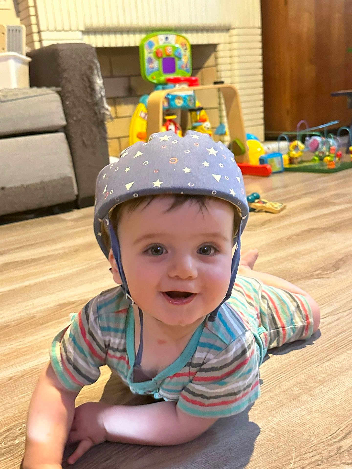 Youenn a rejoint le concours — aidez-le/la à gagner de superbes lots ! baby, helmet, smile, floor, toy, living_room, child, striped_clothing, crawling, happy, indoor, person, face, wooden_floor, play, cute, infant, helmet_pattern, colorful, background