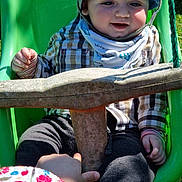 Youenn participe au concours pour gagner de l'argent avec cette photo : toddler, child, swing, hat, plaid_shirt, outdoor, playground, green, sunlight, smile, baby, person, hand, clothing, safety_bar, grass, daylight, play, interaction, park