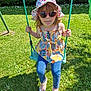 child, swing, hat, sunglasses, grass, outdoor, playground, summer, fun, sunlight, greenery, casual_clothing, jeans, shoes, flower, nature, person, happy, tongue_out, daylight