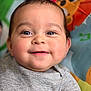 animal_pattern, baby, cheeks, child, close_up, colorful_background, cute, eyes, face, gray_clothing, happy, head, indoors, infant, person, play_mat, portrait, smiling, soft_lighting, young