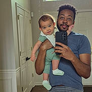 Udaya joined the competition — help win amazing prizes! baby, casual_clothing, child, curly_hair, door, floor, greenery, holding, home, indoor, man, mirror, onesie, person, phone, reflection, selfie, smile, socks, window