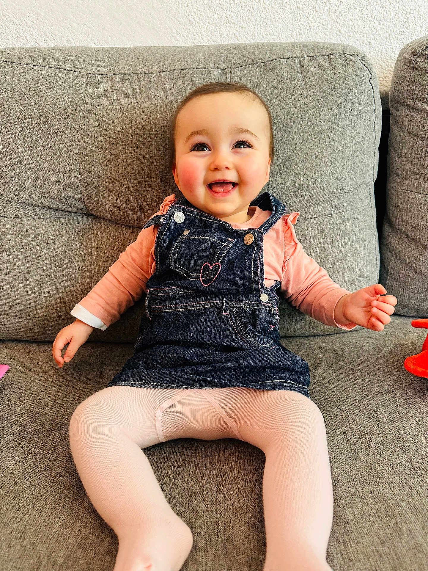 Margot participe au concours pour gagner de l'argent avec cette photo : baby, infant, smile, overalls, denim, pink_tights, couch, sofa, rosy_cheeks, happy, sitting, living_room, textured_wall, cute, portrait, small_hand, legs, plush_toy, eyes, child
