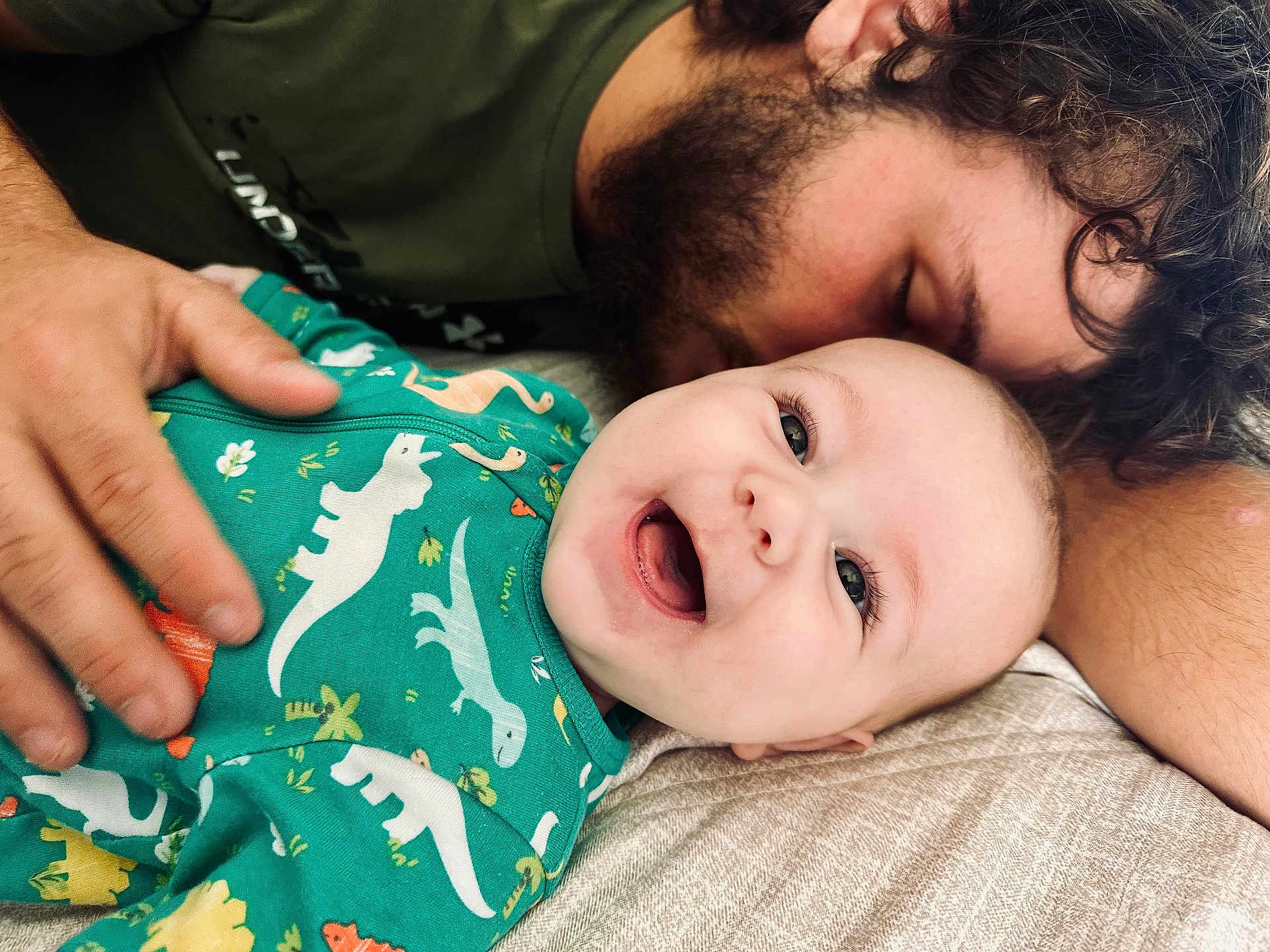 Hudson joined the competition — help win amazing prizes! baby, smile, dinosaur_onesie, beard, adult, hand, bed, happy, closeup, face, skin, cuddle, family, love, infant, joy, portrait, person, lying_down, tenderness