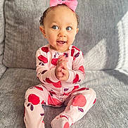 Ariyah joined the competition — help win amazing prizes! apple_pattern, baby, blue_eyes, child, clapping_hands, cozy, cute, gray_couch, happy, indoor, infant, pajamas, pink_bow, playful, portrait, sitting, smiling, soft_texture, toddler, young_child