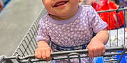 Ariyah is registered to the contest to win money with this photo: baby, child, shopping_cart, headband, smile, happy, clothing, store, aisle, hand, curly_hair, infant, purple_outfit, person, retail, toddler, indoor, cute, holding, face