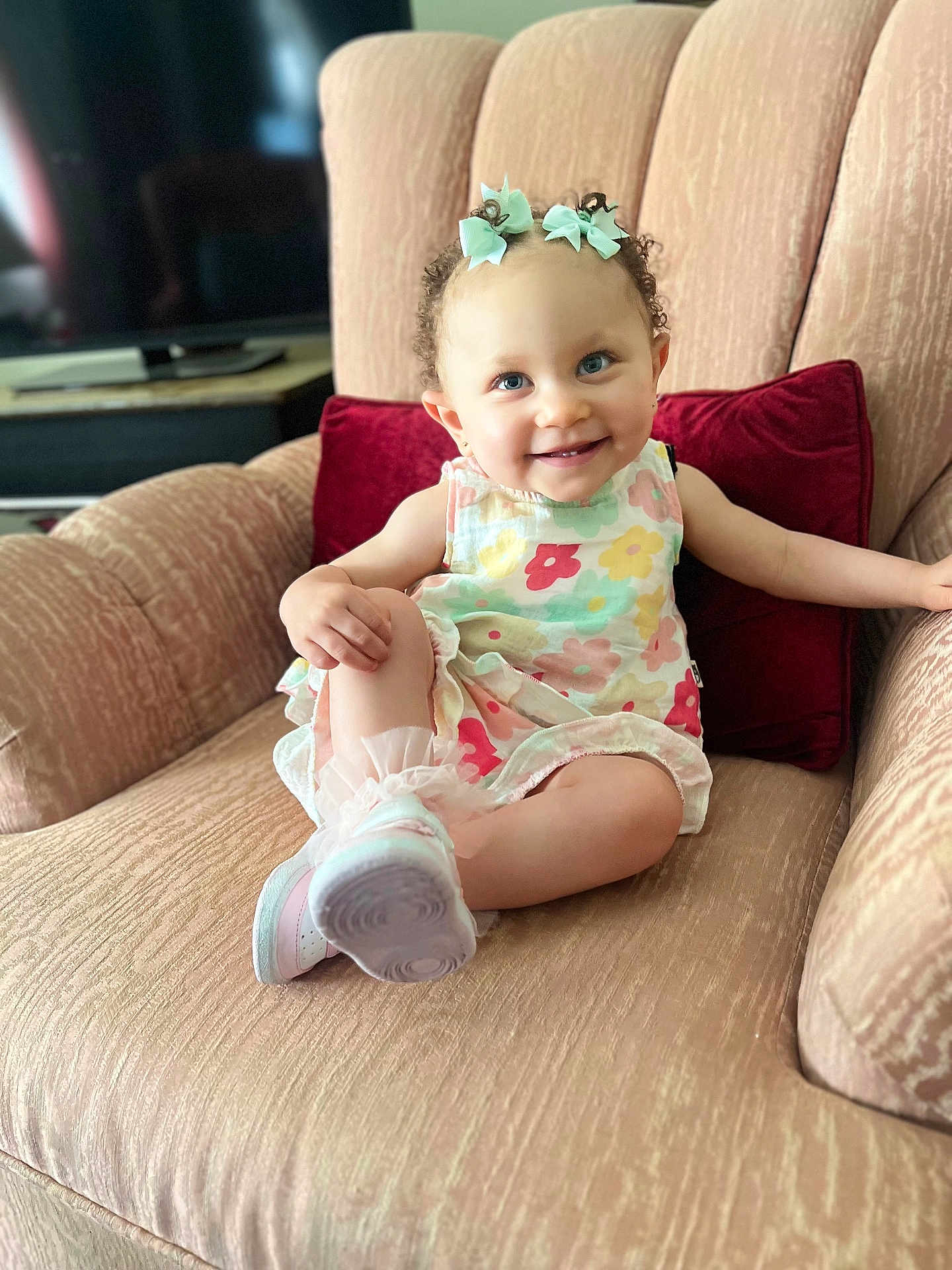 Ariyah is registered to the contest to win money with this photo: toddler, child, smiling, dress, bows, curly_hair, socks, shoes, couch, living_room, pillow, happy, sitting, person, indoor, furniture, cute, portrait, baby, colorful