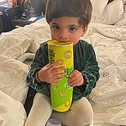 Iman is registered to the contest to win money with this photo: toddler, child, bed, blanket, snack_container, sitting, indoors, curly_hair, cute, clothing, toy, hand, face, eyes, lamp, pillow, carpet, room, plastic_bag, candid