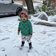 Ibrahim is registered to the contest to win money with this photo: child, snow, winter_clothing, hoodie, gloves, hat, footprints, snowy_driveway, car, house, tree, outdoor, cold_weather, smiling, playful, pants, sneakers, green_hoodie, colorful_hat, snow_covered
