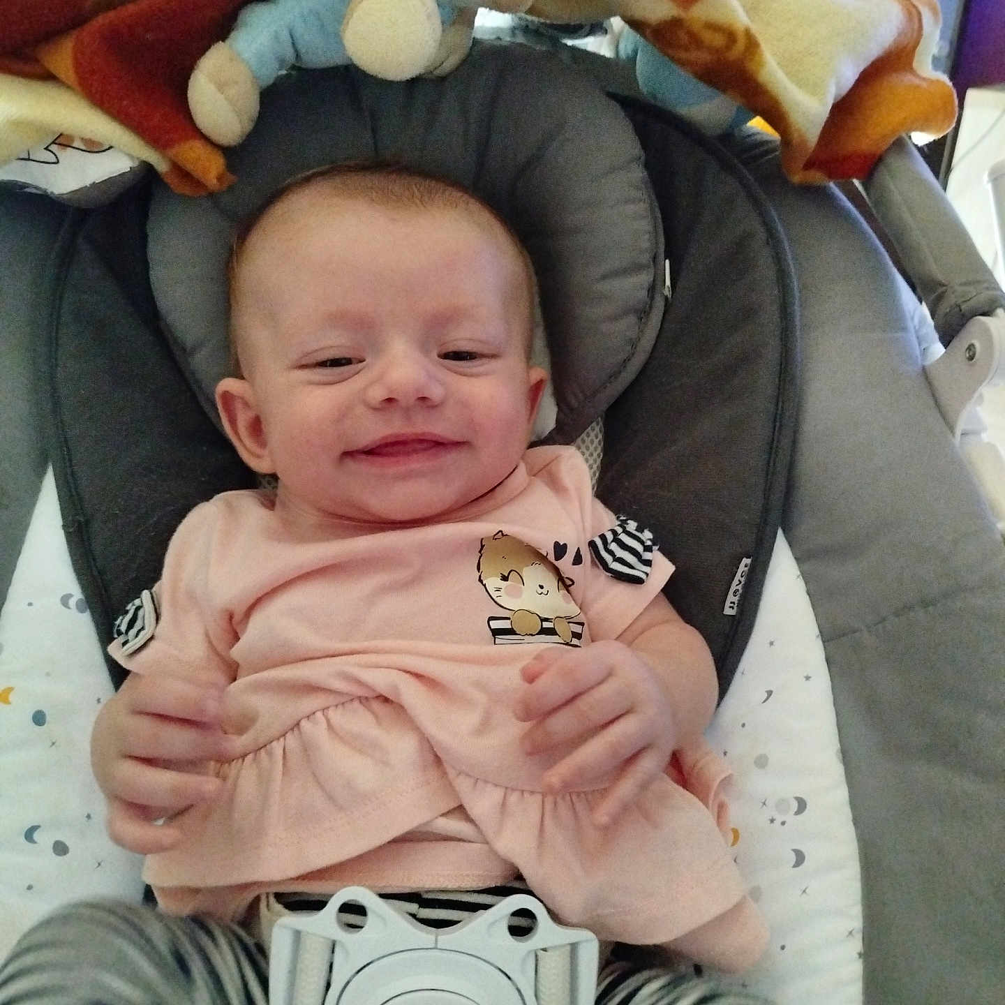 Inaya participe au concours pour gagner de l'argent avec cette photo : baby, baby_rocker, blanket, child, clothing, comfort, cushion, cute, face, happy, head, indoor, infant, person, pink_shirt, plush_toy, resting, seat, smiling, striped_pants