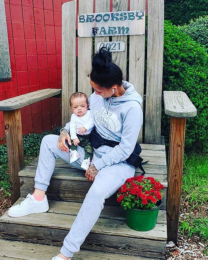 Keyvon is registered to the contest to win money with this photo: child, flower, flowerpot, grass, happy, hat, human_leg, jeans, lap, leaf, leg, leisure, outerwear, person, plant, public_space, shoe, sitting, smile, sneakers