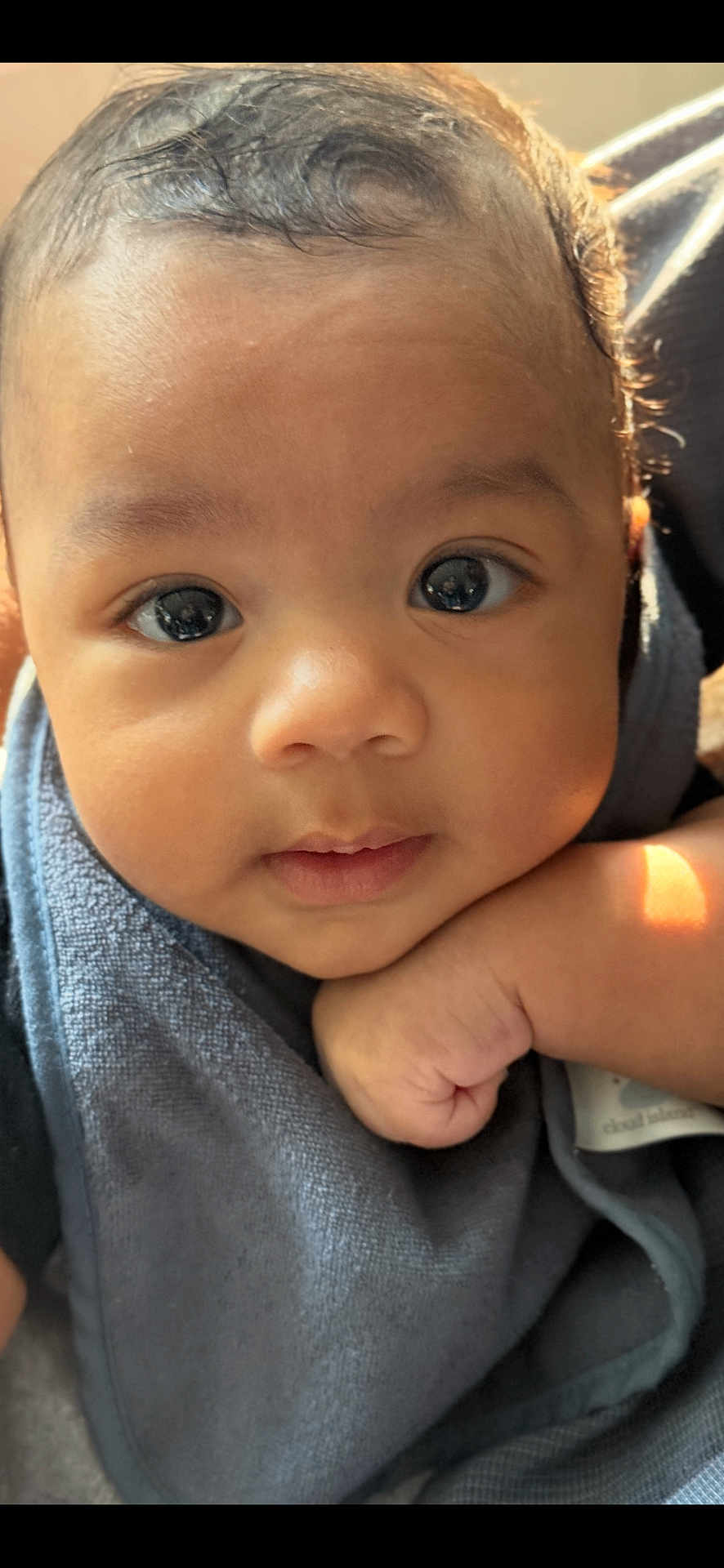 Ocean is registered to the contest to win money with this photo: baby, close_up, face, eyes, hand, infant, skin, hair, expression, resting, curious, blue_cloth, cozy, sunlight, soft_texture, portrait, child, cute, peaceful, young