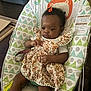 baby, child, infant, bouncer, dress, hair_clip, patterned_clothing, bracelet, indoor, flooring, wood_floor, baby_seat, colorful, cute, person, face, hands, expression, furniture, toy