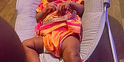 Cimani is registered to the contest to win money with this photo: baby, child, smiling, orange_clothing, baby_rocker, indoor, floor, wooden_floor, infant, bracelet, diaper, seat, toy, happy, person, cute, young_child, playful, relaxed, home