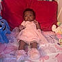 baby, infant, bed, pillow, pink_dress, booties, plush_toy, stuffed_animal, butterfly_pattern, crib, child, toddler, soft_toys, sleeping_area, room, cute, portrait, indoor, laying_down, expression