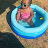 toddler, child, pool, inflatable_pool, sunglasses, swimsuit, outdoor, grass, summer, water, toy_duck, shadow, sunlight, playing, fun, baby, cute, fashion, relaxing, sunny_day