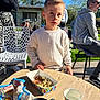 child, boy, outdoor, table, snacks, party, popcorn, cup, people, sweater, sunlight, grass, chair, adult, conversation, daylight, casual_clothing, party_food, relaxing, background