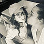 child, adult, glasses, cap, kiss, affection, black_and_white, indoor, chair, table, person, long_hair, casual_clothing, closeup, face, love, family, home, portrait, interaction