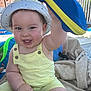 baby, child, smiling, hat, yellow_overalls, outdoor, towel, inflatable_toy, playful, happy, skin, face, arm, hand, summer, sun_hat, baby_clothes, person, seat, daylight