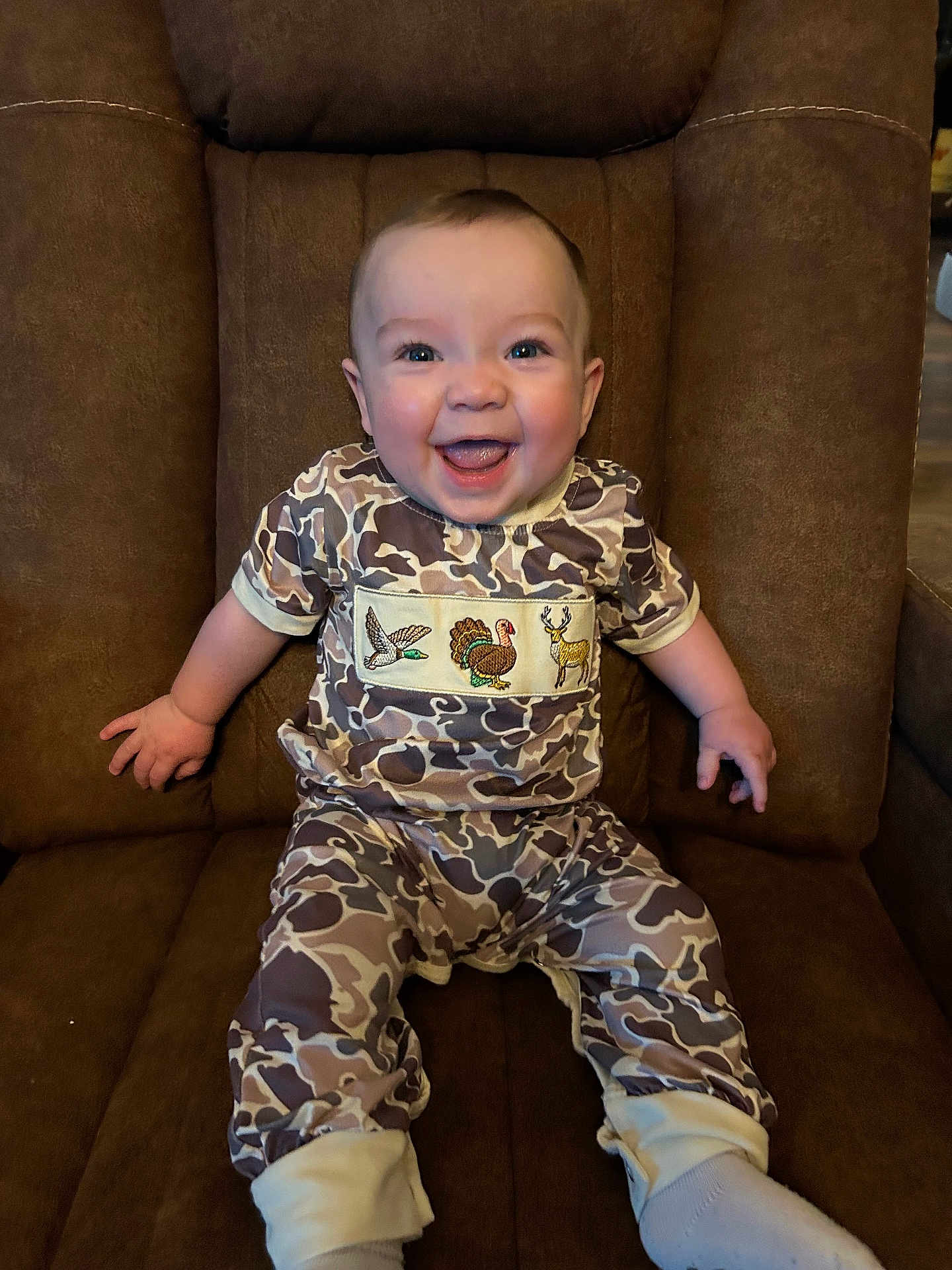 Walker joined the competition — help win amazing prizes! baby, child, smiling, camo_clothing, chair, brown_furniture, happy, sitting, cute, infant, portrait, indoors, person, young_child, embroidered_clothing, cozy, comfortable, bright_eyes, small_hands, soft_lighting