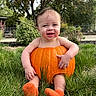 autumn, baby, booties, child, face, family_photo, garden, grass, halloween, happy, infant, knitted_shoes, nature, orange, outdoor, portrait, pumpkin, pumpkin_costume, sitting, smiling