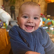 Averino a rejoint le concours — aidez-le/la à gagner de superbes lots ! baby, smiling, child, blue_jacket, indoor, cozy, happy, face, person, cute, infant, fleece, playful, closeup, portrait, hand, toy, blurred_background, warm_lighting, cheerful