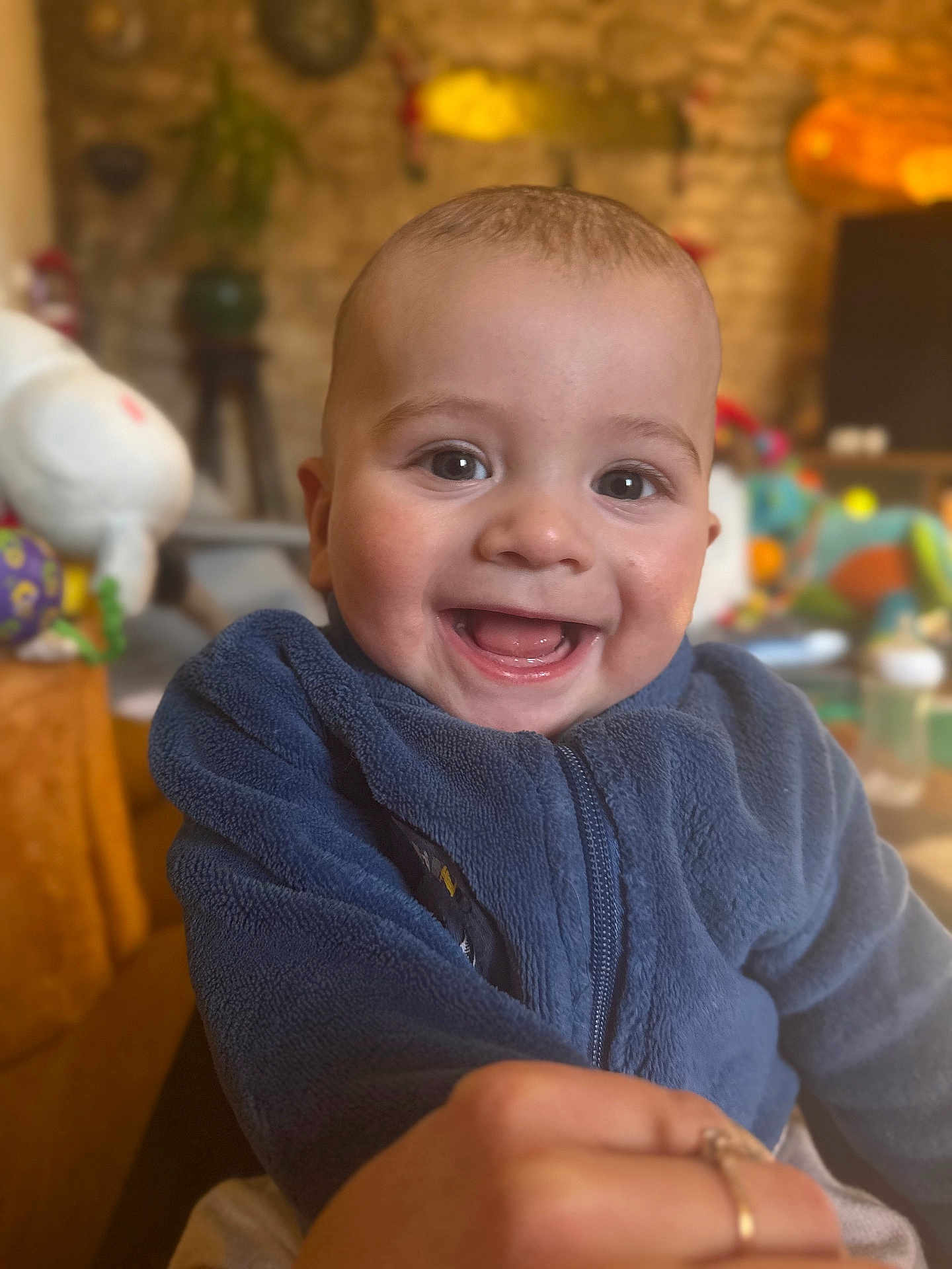 Averino a rejoint le concours — aidez-le/la à gagner de superbes lots ! baby, smiling, child, blue_jacket, indoor, cozy, happy, face, person, cute, infant, fleece, playful, closeup, portrait, hand, toy, blurred_background, warm_lighting, cheerful