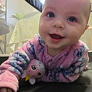 Joanna is registered to the contest to win money with this photo: baby, child, close_up, cozy, curious, eyes, face, happy, indoors, infant, laying, mouth, onesie, pajamas, pink_clothing, playpen, plush_toy, smiling, soft_texture, stuffed_animal