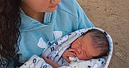 Caden is registered to the contest to win money with this photo: child, baby, newborn, blanket, outdoor, person, holding, curly_hair, hoodie, blue_clothing, sleeping, infant, young_girl, casual_clothing, vehicle, dirt_ground, tender_moment, wrapped, peaceful, family