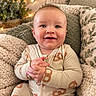 Stetson is registered to the contest to win money with this photo: baby, child, infant, smiling, portrait, sitting, indoors, couch, pillows, blanket, fairy_lights, plant, cozy, warm_lighting, onesie, patterned_clothing, hands, face, happy, home_decor