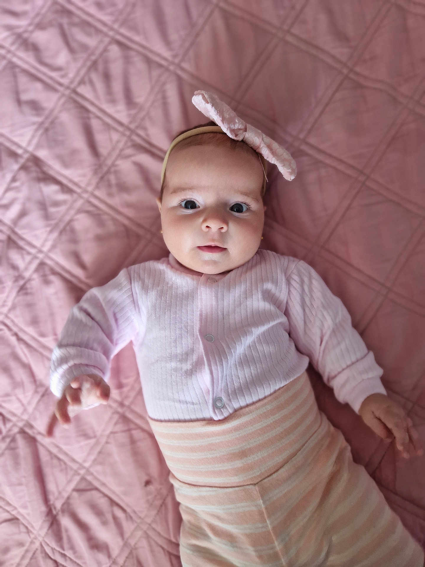 Melissa participe au concours pour gagner de l'argent avec cette photo : baby, child, infant, pink, headband, bow, striped_pants, quilt, bed, blanket, soft_texture, looking_at_camera, cute, clothing, portrait, hand, lying_down, indoors, person, adorable