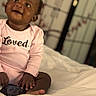 Kailani joined the competition — help win amazing prizes! baby, child, infant, smiling, pink_onesie, loved_text, smartphone, bed, white_bedspread, indoor, portrait, happy, cute, sitting, face, hands, feet, black_skin, decorative_screen, blurred_background