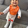 toddler, child, smiling, orange_vest, hair_bow, white_shirt, white_pants, white_shoes, carpet, couch, indoor, happy, cute, standing, person, baby, fashion, earrings, home, portrait