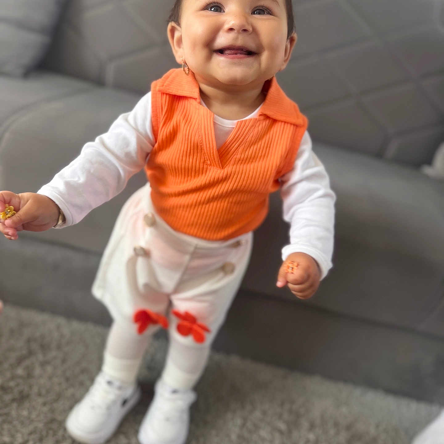 Leyla joined the competition — help win amazing prizes! baby, carpet, child, couch, cute, earrings, fashion, hair_bow, happy, home, indoor, orange_vest, person, portrait, smiling, standing, toddler, white_pants, white_shirt, white_shoes