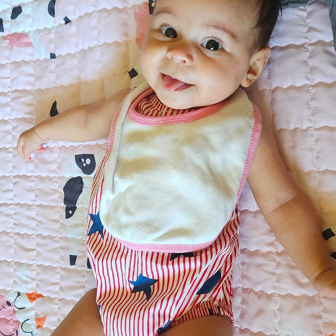 Rye joined the competition — help win amazing prizes! animal_pattern, arm, baby, bib, cheerful, child, cute, face, happy, head, indoor, infant, lying_down, person, pink, quilt, skin, smiling, striped_clothing, tongue_out