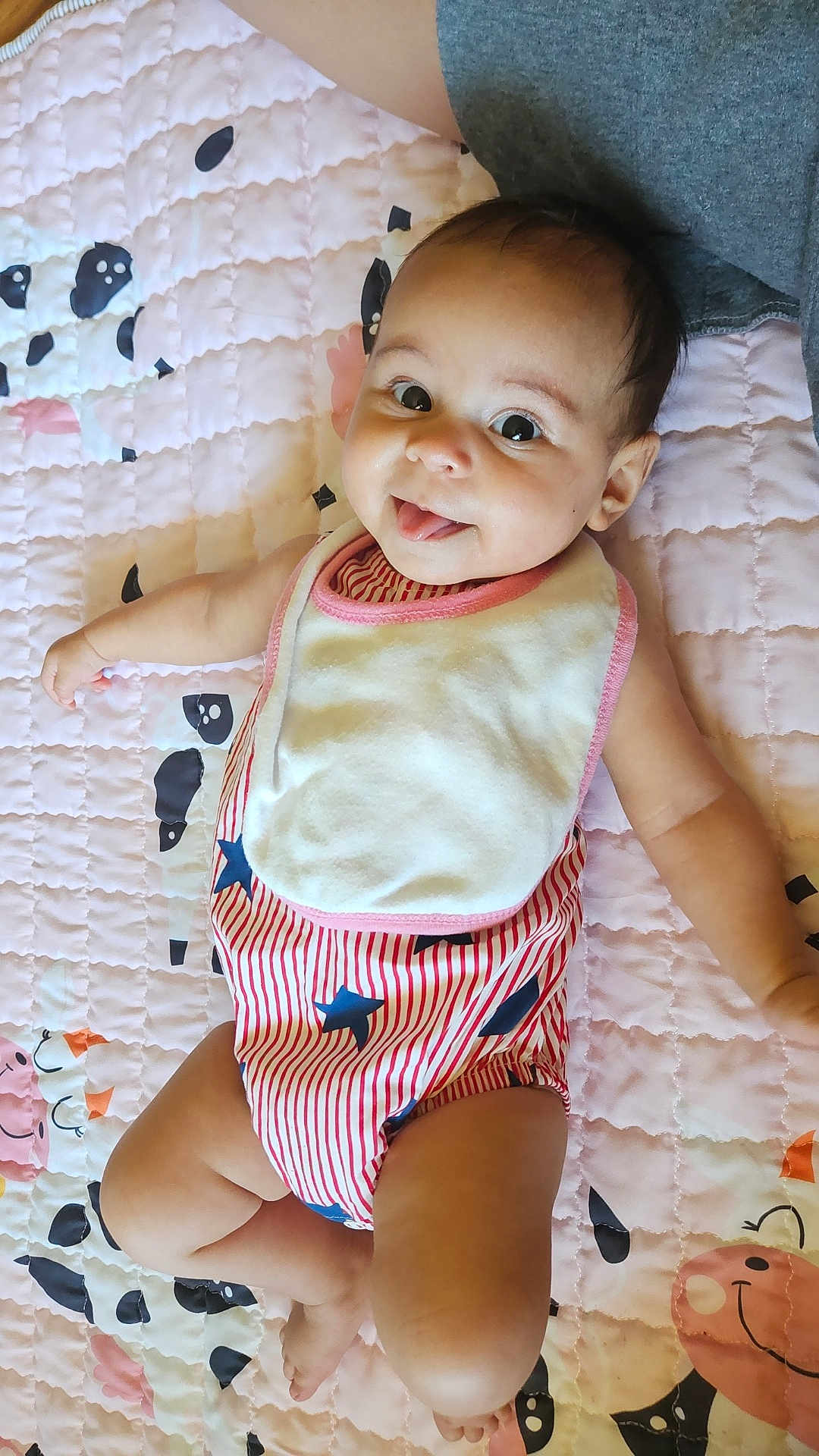 Rye joined the competition — help win amazing prizes! baby, child, infant, smiling, tongue_out, striped_clothing, bib, quilt, pink, animal_pattern, lying_down, cute, happy, cheerful, indoor, person, skin, head, face, arm