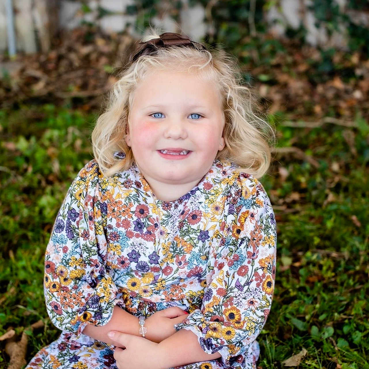 Emilyn joined the competition — help win amazing prizes! blonde_hair, blue_eyes, bracelet, casual, child, curly_hair, daylight, fall_leaves, floral_dress, girl, grass, greenery, happy, long_sleeves, nature, outdoor, portrait, sitting, smiling, young_child